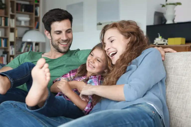 Gezin zit op de bank - de vader links, hun dochter in het midden en de moeder rechts