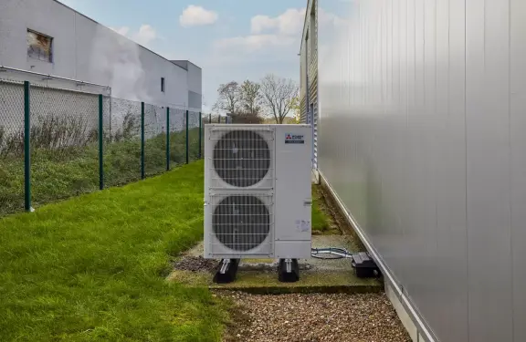 Witte buitenunit staat naast wit gebouw met gras daarrond