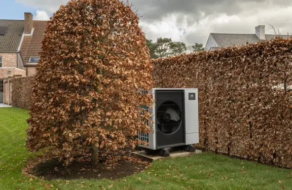 Warmtepomp achter een struik in de tuin