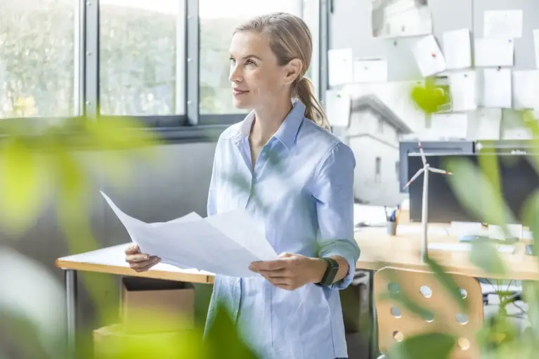 Vrouw die aan het denken is aan haar ondernemersideeën terwijl ze een blad vast houdt.