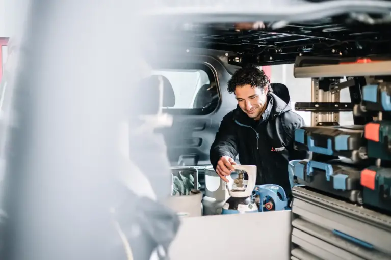 Installateur met zwarte jas pakt een fles uit zijn bestelwagen